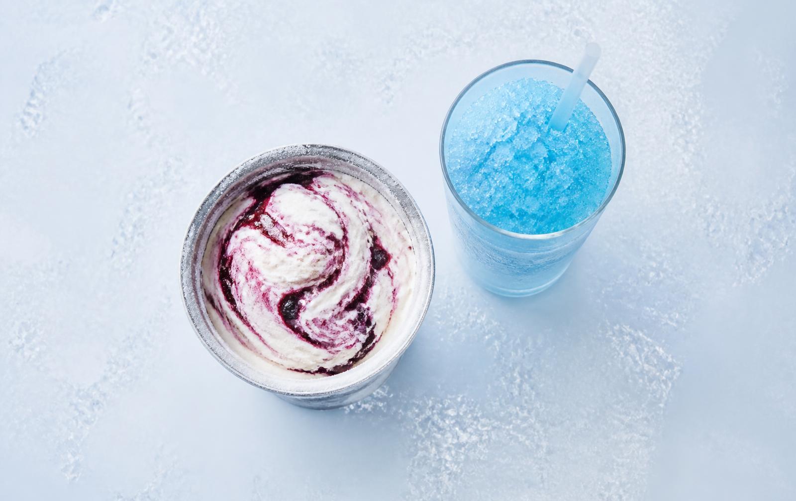 A pint of swirled ice cream beside a glass of blue slush